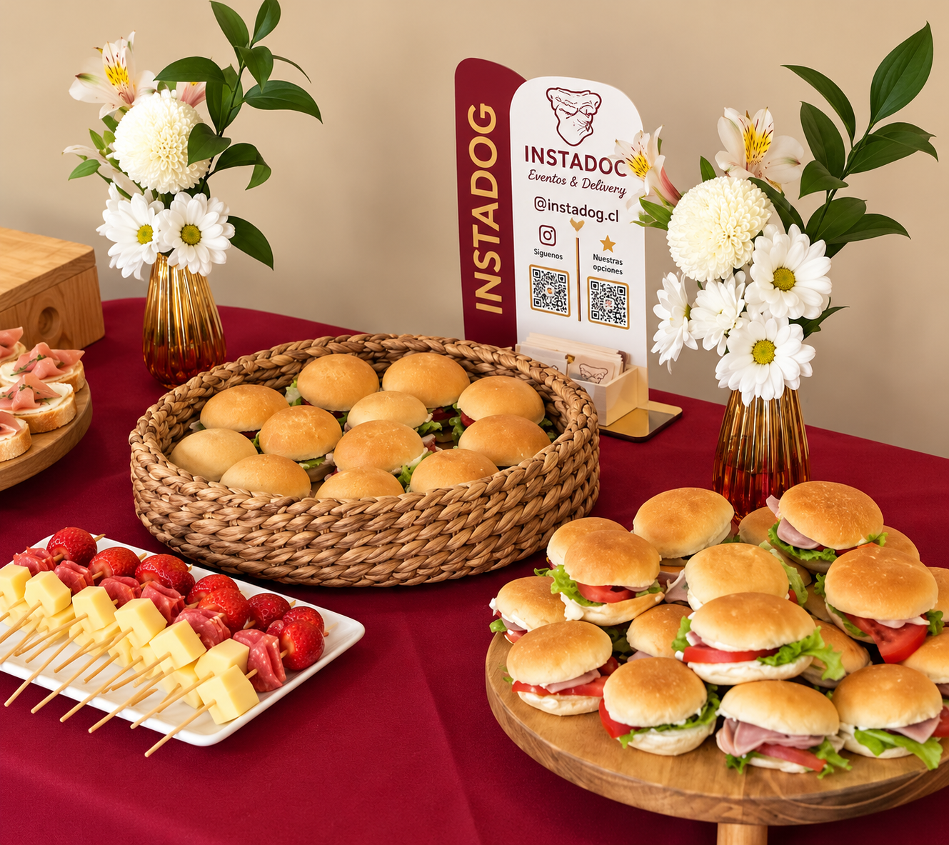 Mini sándwiches y pastelería sobre mantel burdeo con flores blancas